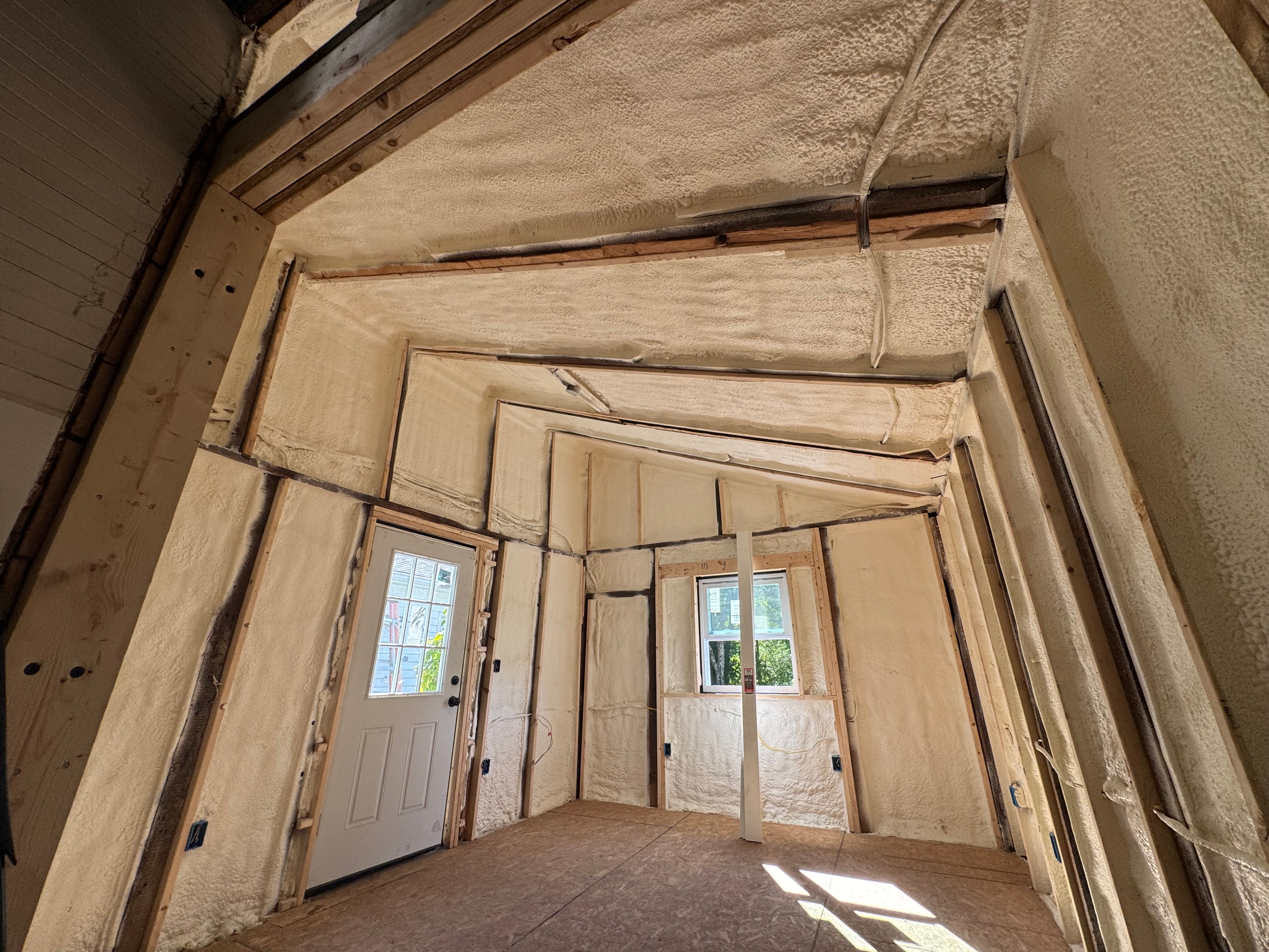 Spray foam insulation covering walls and ceiling of a garage conversion